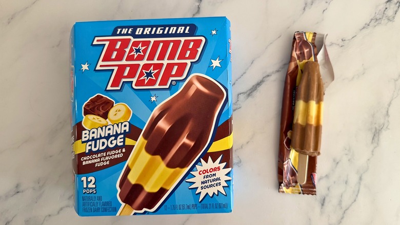 Box of Banana Fudge Bomb Pops next to opened Bomb Pop on marble surface
