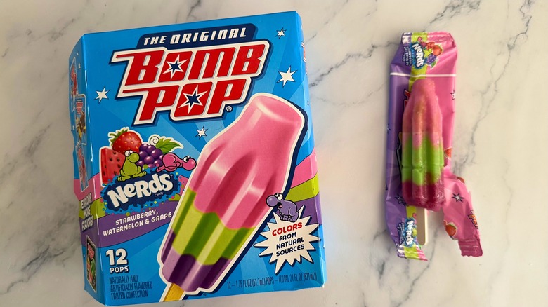 Box of Nerds Bomb Pops next to opened Bomb Pop on marble surface