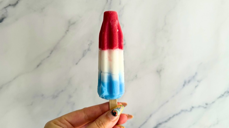 Hand holding Original Bomb Pop in front of marble background