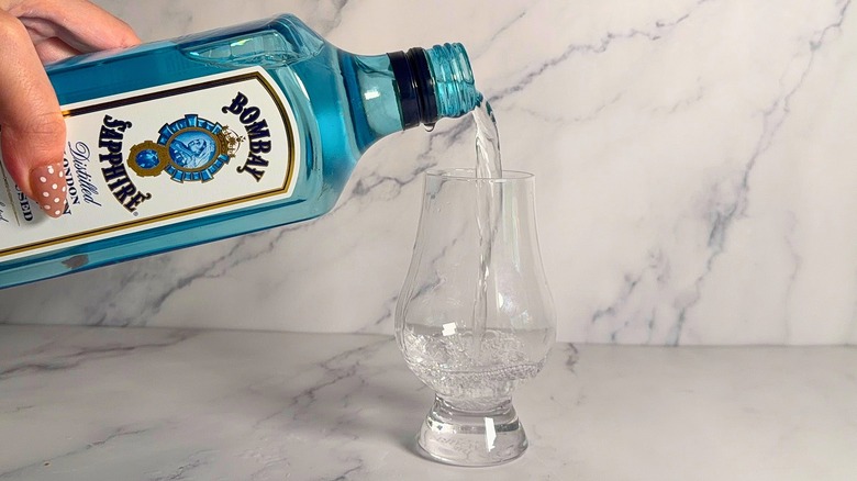 Hand pouring bottle of Bombay Sapphire into glencairn glass on marble surface