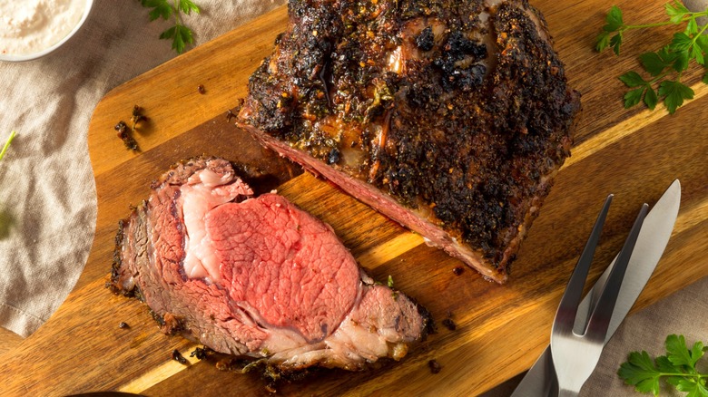 Cooked boneless prime rib roast next to slice on wooden cutting board