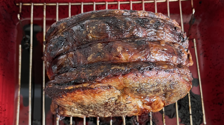 Whole boneless cooked prime rib roast on silver roasting rack above red roasting pan