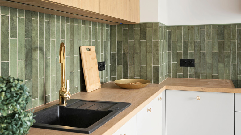 kitchen sink with tap, contemporary green tile on the wall, and wooden counter