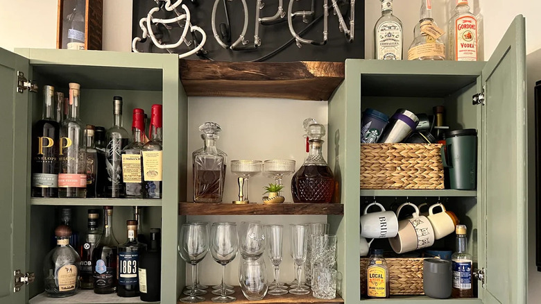 close up of stocked home bar with an open sign and green cabinets