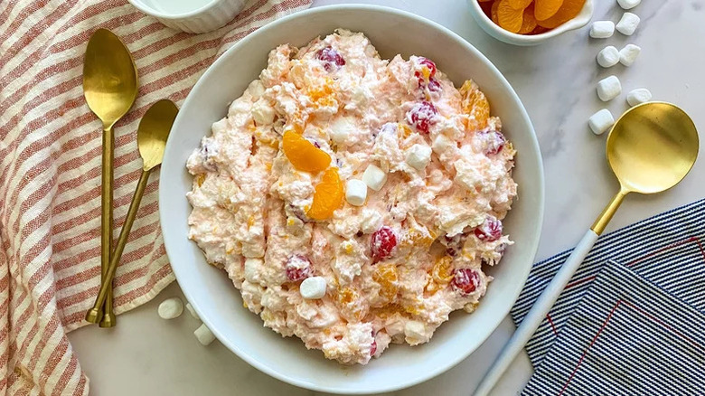 Bowl of ambrosia salad on a marble counter with tea towels, utensils, and ingredients around it