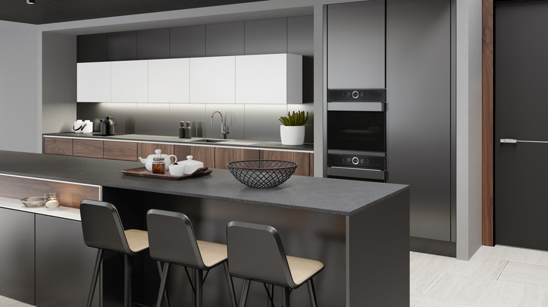 An extremely modern, minimalist kitchen, with dark cabinetry and an island, looking very austere and showcase-perfect