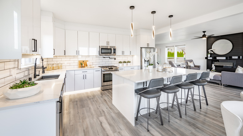 A large, sleek, modern, all-white kitchen, where the work triangle has been compromised by placing the sink well outside of the cooking area