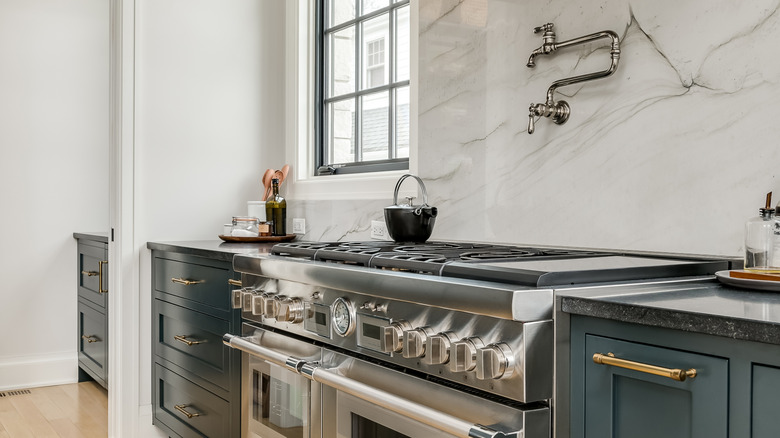 A modern, designer kitchen, with dark cabinetry and countertops, a marble-looking backsplash, and a pot-filler faucet over the gas range