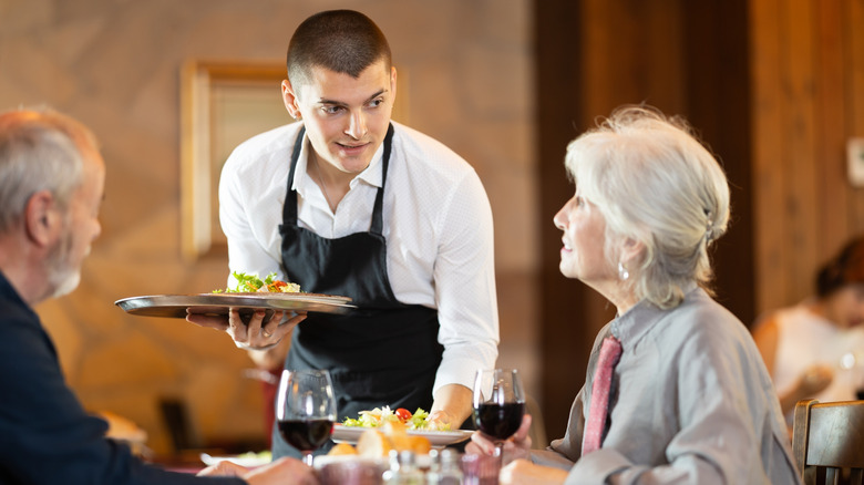 A waiter with a tray serving an elderly couple at a restaurant