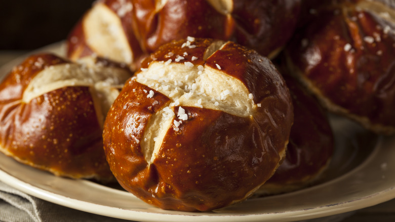 Salted pretzel buns on a cream plate.