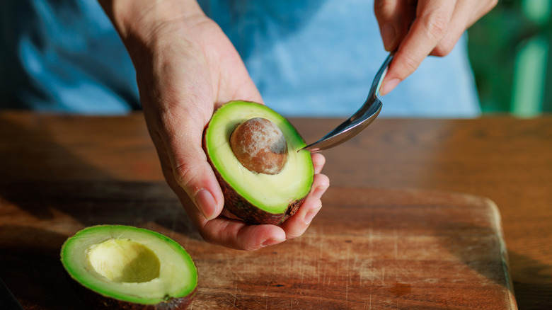 a person holding half a cut avocado and wielding a spoon