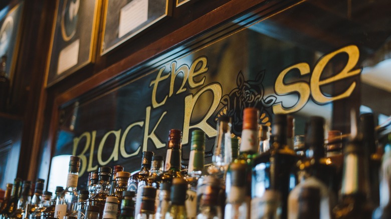 Mirrored bar sign with The Black Rose written on it in gold and rows of liquor bottles in front of it