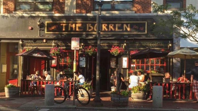 Facade of bar with black and gold The Burren sign, red trimmed windows and an outdoor seating area