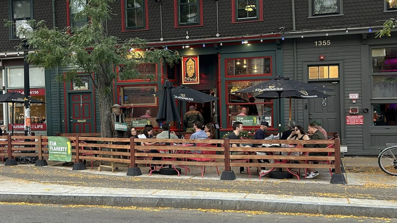 exterior shot of two story Druid pub dark grey facade trimmed in red and green, outdoor seating area