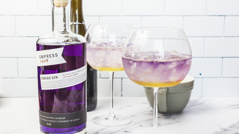 Two glasses of layered lavender spritz cocktail, with gin and prosecco in background.