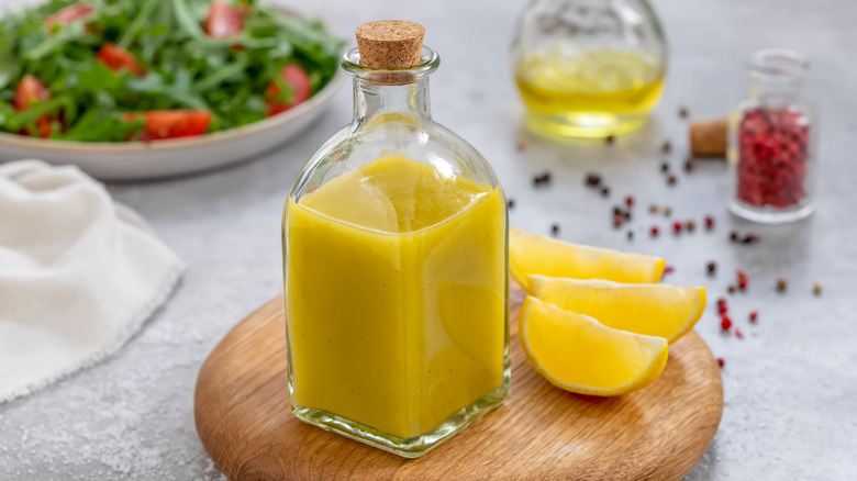 Lemon vinaigrette in a glass bottle with fresh lemon wedges and peppercorns on a cutting board