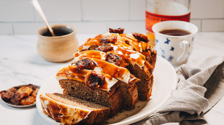 Bourbon banana bread on platter with banana slices, bourbon sauce, tea, and a bourbon bottle.