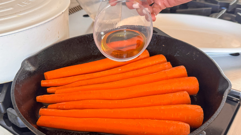 pouring bourbon over carrots in pan
