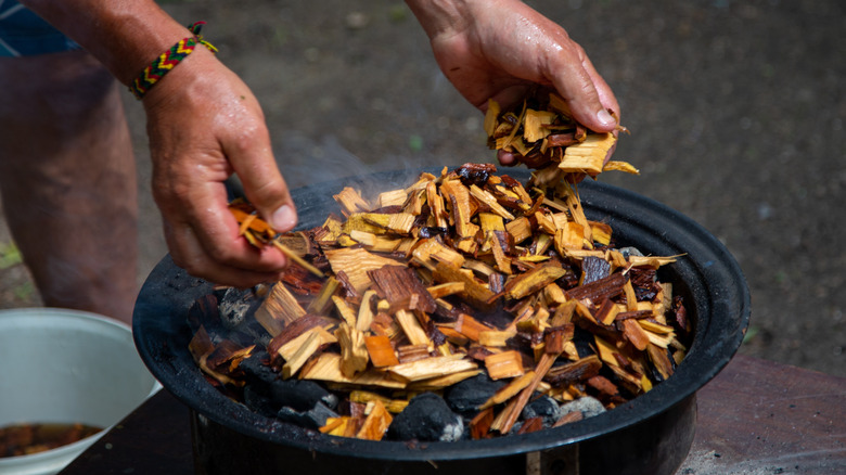 hands adding wood chips to smoker