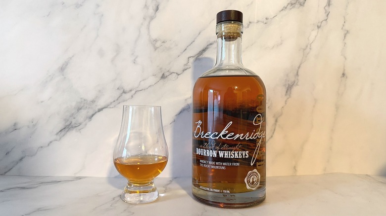 Bottle of Breckenridge bourbon next to glencairn of bourbon on marble background