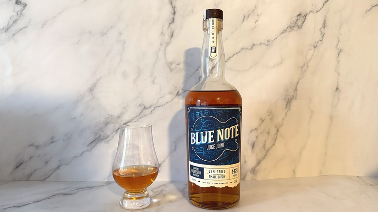 Bottle of Blue Note bourbon next to glencairn of bourbon on marble background