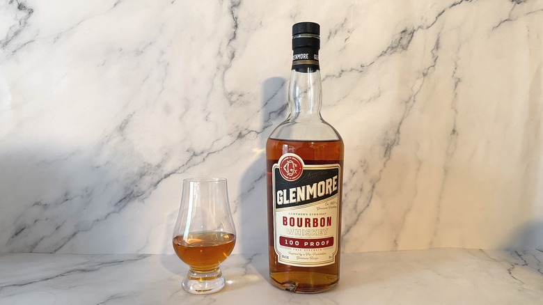 Bottle of Glenmore bourbon next to glencairn of bourbon on marble background