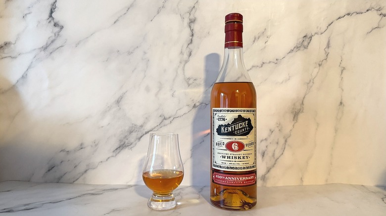 Bottle of Kentucke County bourbon next to glencairn of bourbon on marble background