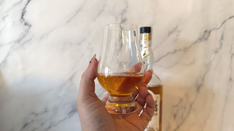 Hand holding glencairn of bourbon in front of bottle of bourbon on marble background