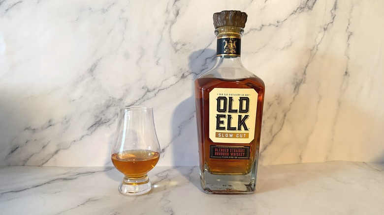 Bottle of Old Elk bourbon next to glencairn of bourbon on marble background