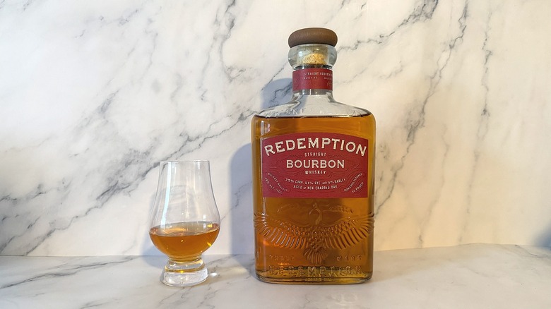 Bottle of Redemption bourbon next to glencairn of bourbon on marble background