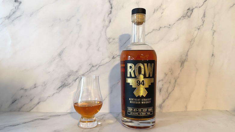 Bottle of Row 94 bourbon next to glencairn of bourbon on marble background