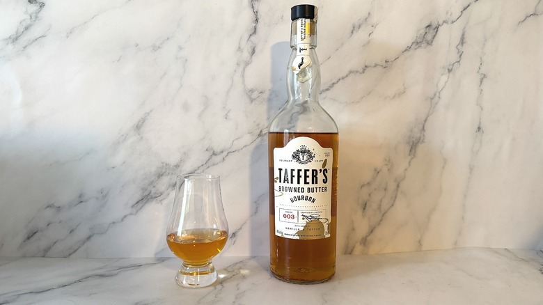 Bottle of Taffer's bourbon next to glencairn of bourbon on marble background