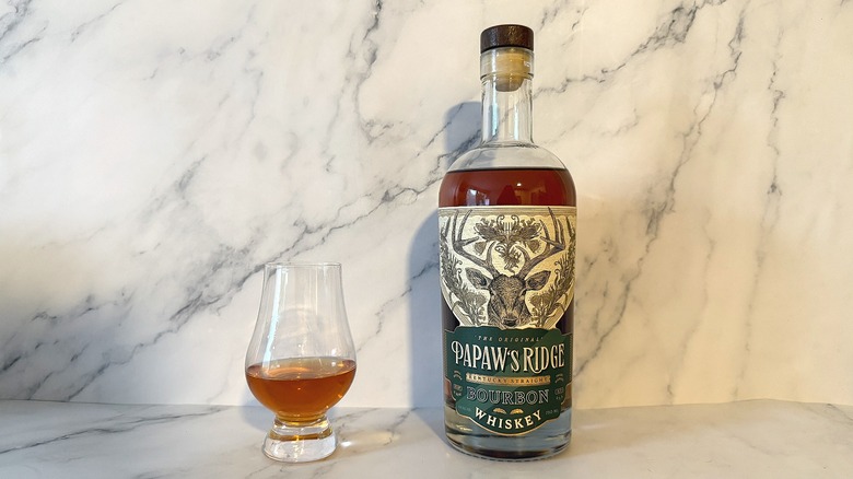 Bottle of Papaw's Ridge bourbon next to glencairn of bourbon on marble background