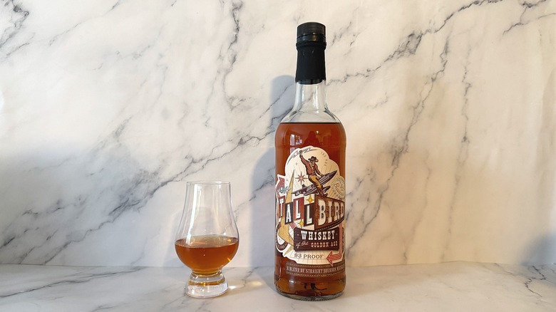 Bottle of TallBird bourbon next to glencairn of bourbon on marble background