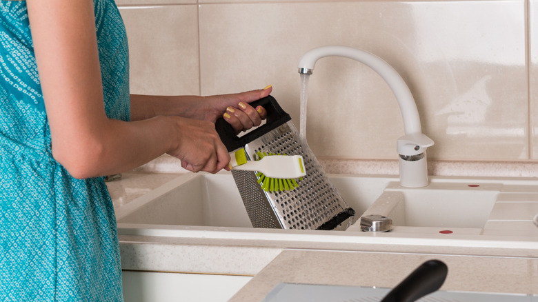 Woman washing a box grater in her kitchen sink with a brush