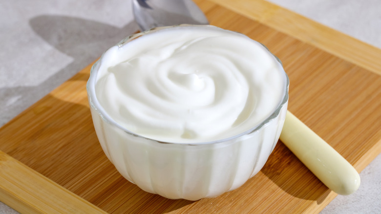 Greek yogurt in a bowl on a wooden tray with a spoon
