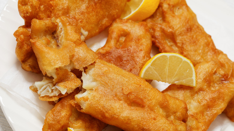 Close-up of beer battered fish on plate with lemon wedges