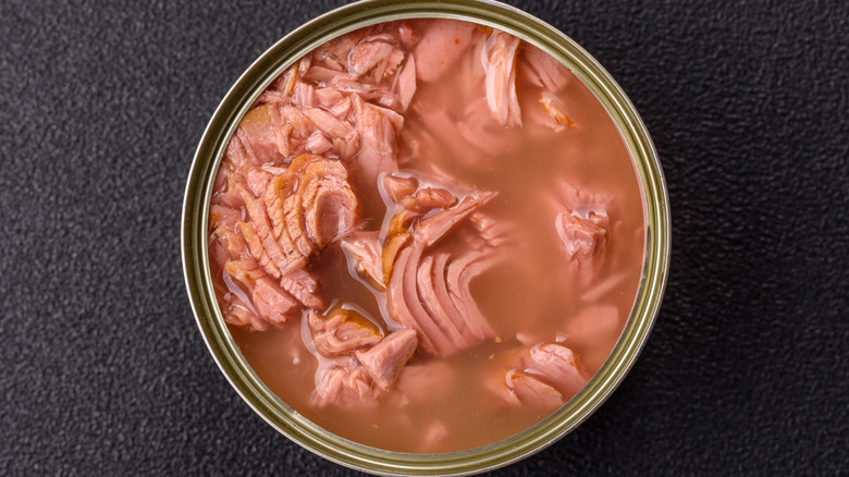 Aerial shot of tuna in a can with brine on black surface