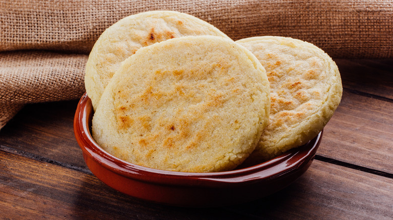 Arepas in a red bowl on a wooden tabletop