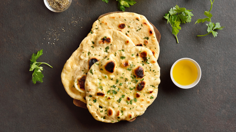 Top-down view of a pile of naan breads next to a bowl of melted butter and sprigs of fresh coriander