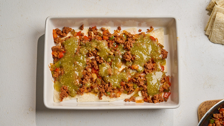 salsa verde in a casserole dish with chorizo and tortillas