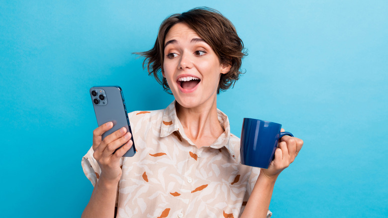 A person holding a mug and a cell phone