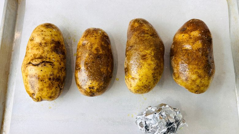 Oiled potatoes and foil ball on baking sheet