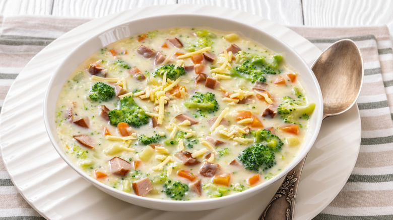 Bowl of sausage potato chowder with black pepper bits and white cheese, crusty bread, wooden background
