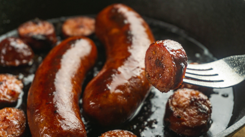 Smoked sausages whole frying and sliced browning in cast iron skillet