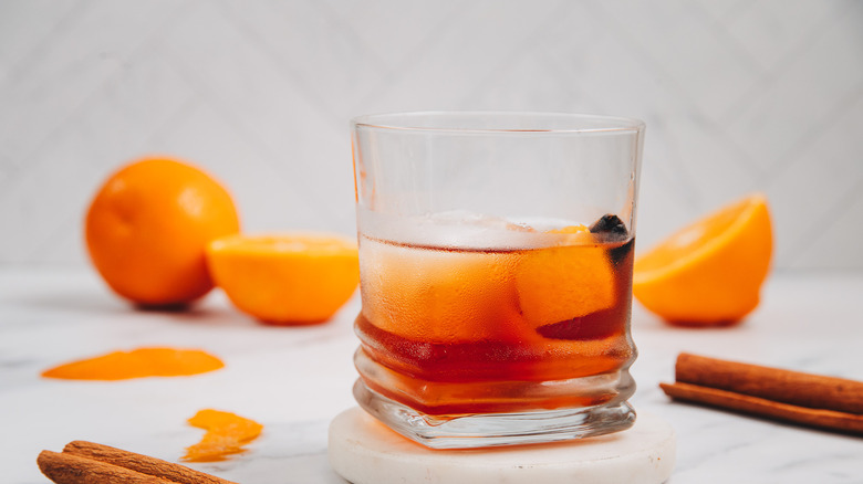 A glass of a brown butter old fashioned with oranges in background