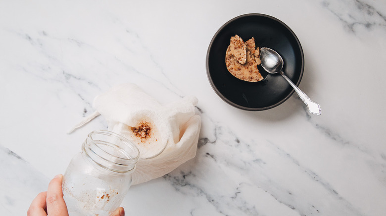 Straining brown butter bourbon into jar over cheesecloth