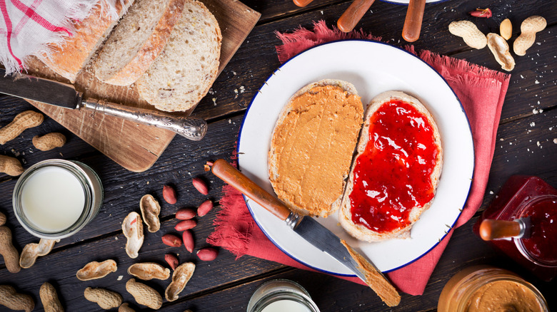 A peanut butter and jelly sandwich on a plate, alongside jars of peanut butter and jelly and a sliced loaf of bread