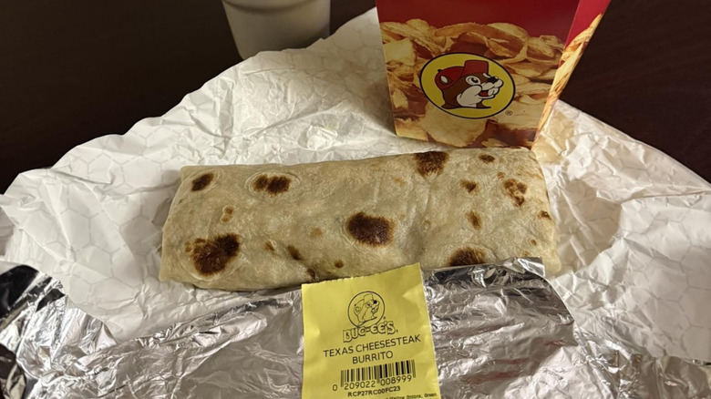 an unwrapped Buc-ee's Texas Cheesesteak Burrito next to a chips container