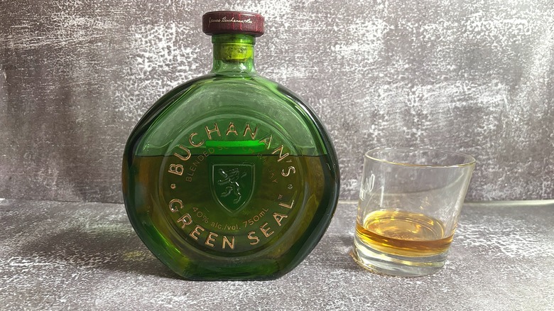 Green bottle of Buchanan's Green Seal next to glass of whisky on black background